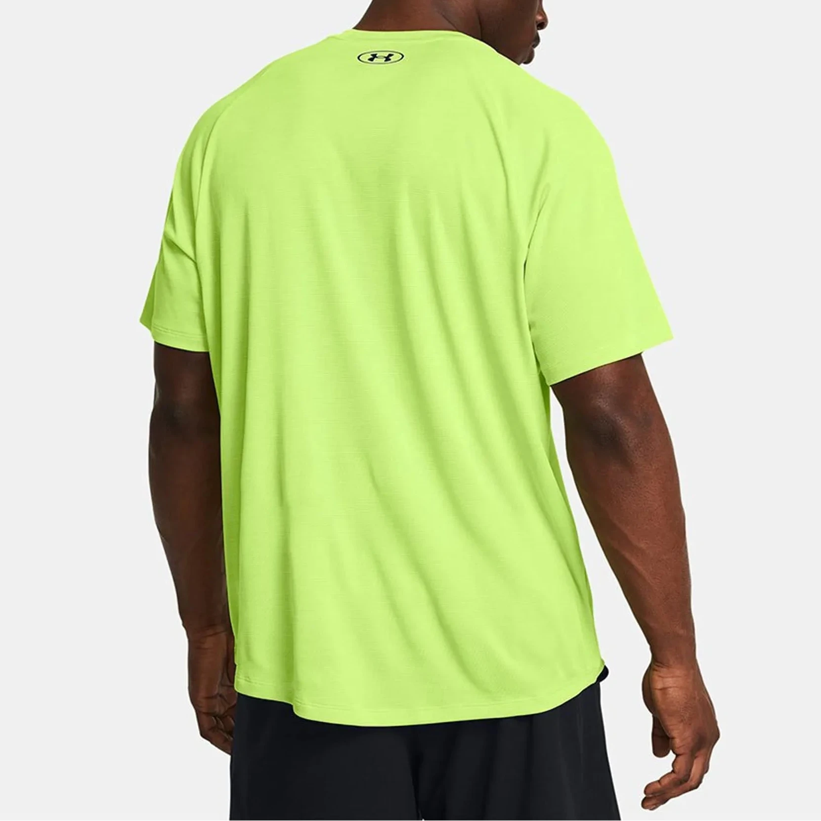 Person wearing a bright green t-shirt with a brand logo on the back, on a white background