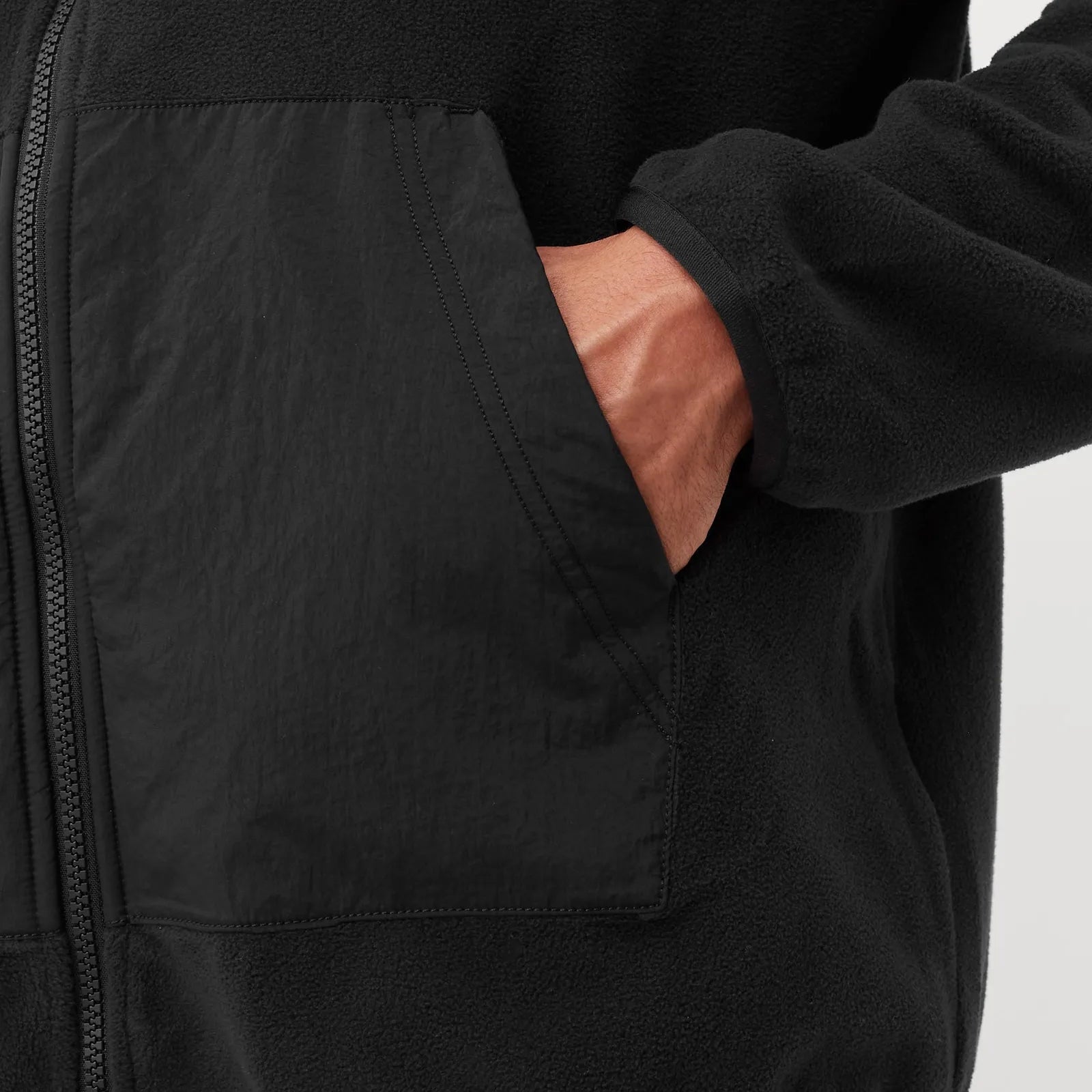 Close-up of a black jacket with a pocket showing pink lining on a light gray background